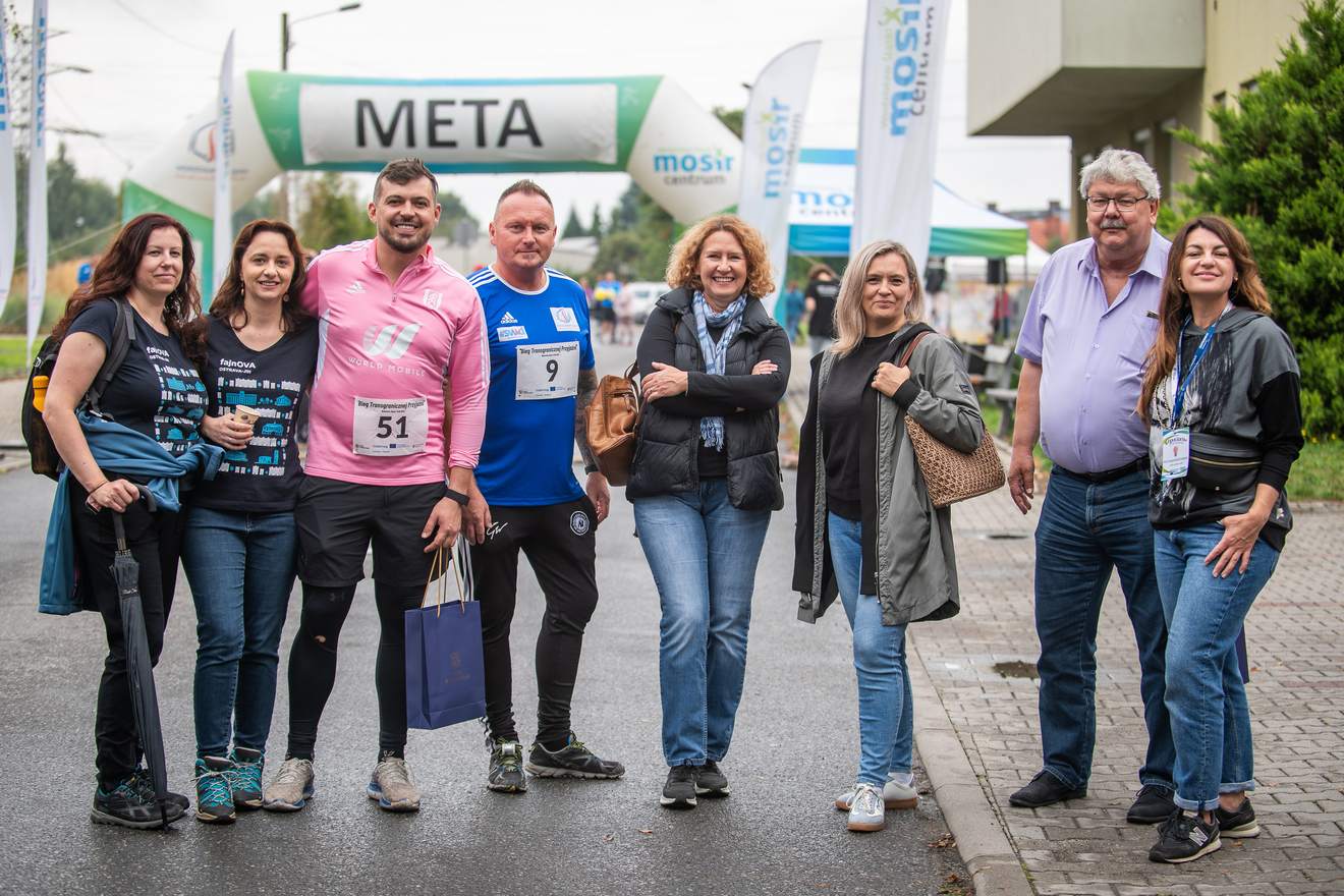 Grupa gości i uczestników pozuje pod bramą z napisem META